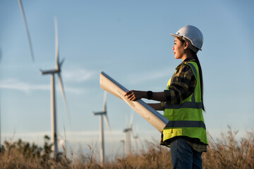 Woman engineers with drawing against turbines on wind turbine farm.