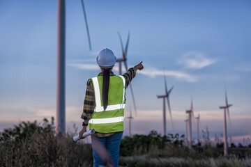 Woman engineers with drawing against turbines on wind turbine farm.