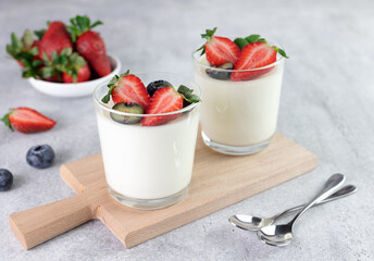 Panna cotta in glass with fresh berries - strawberries and blueberries on a gray background. Italian dessert