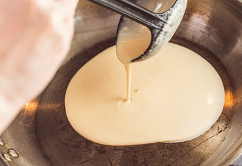 A woman's hand pours pancake batter into a hot pan. Recipe Crepe Suzette. Close-up, chosen focus