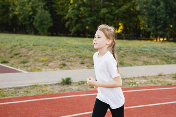 Child girl athlete runs on a track. Concept of sport, fitness, achievements, studying.