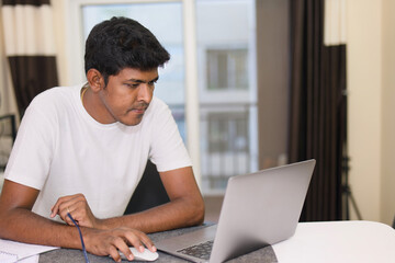 Young indian man using laptop computer in the living room at home work from home concept