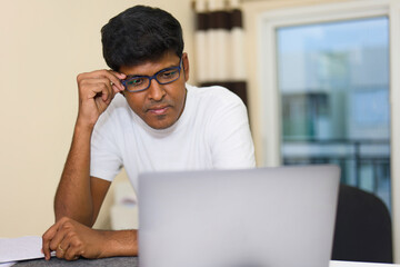 Indian male in eyeglasses working on laptop computer at home