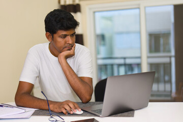 indian young man working at home with laptop computer and notepad