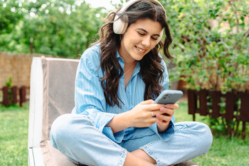 One young caucasian woman is relaxing in easy chair in her backyard while using her phone and...