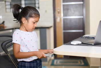 Cute little girl adjusting a laptop computer table height in the kitchen at home