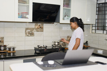 Young woman cooking in the kitchen at home using her laptop computer