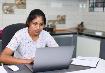 indian woman working at home with laptop computer and notebook in kitchen