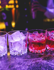 Bartender working, beautiful row line of different coloured liquor alcohol cocktails on a party in a bar, and others on catering banquet on event, barman mixing drinks and beverages in a club