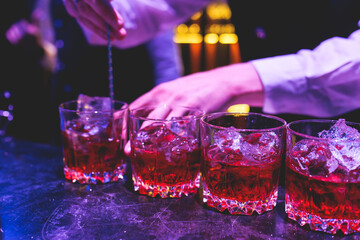 Bartender working, beautiful row line of different coloured liquor alcohol cocktails on a party in...