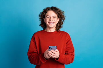 Photo of cheerful positive guy dressed red pullover communicating modern gadget isolated blue color...