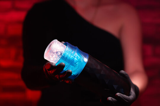 Sex toys for men. A male automatic telescopic masturbator in the hands of a girl in black latex gloves and a black dress on a red background. Male massager. Sex shop Adult store, toys for two
