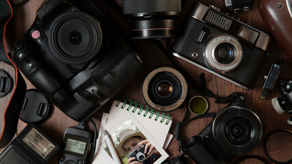 Photograph of young woman taking a photo, surrounded by flash, filters, lenses, modern and old cameras on a wooden table