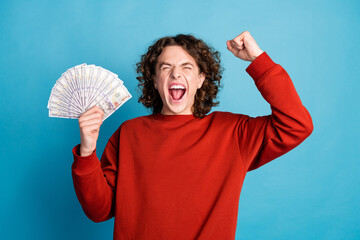 Photo of lucky cool guy dressed red pullover rising fish winning cash fan emtpy space isolated blue...