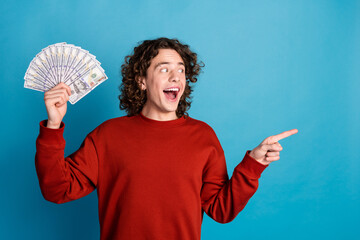 Photo of impressed positive guy dressed red pullover rising money fan pointing emtpy space isolated...
