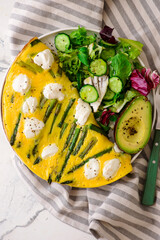 Omelet with asparagus and goat cheese on a plate with avocado and green salad