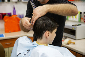 hairdresser cutting boy's hair in a barbershop	