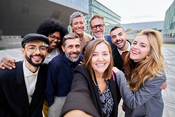 Cheerful group of multiracial business people taking a selfie together outside office building, looking at the camera smiling.