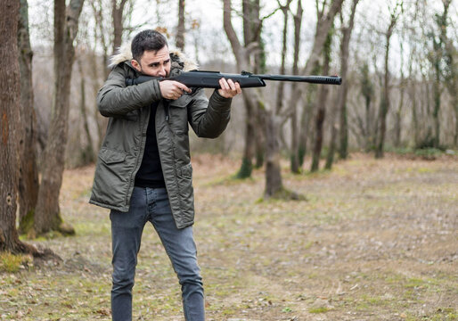 Young man aims and shoots with rifle in woodland