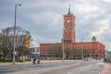 Fototapeta premium The iconic Red City Hall in Berlin stands out against a cloudy sky as evening falls, with city life bustling in the foreground. Berlin, Germany