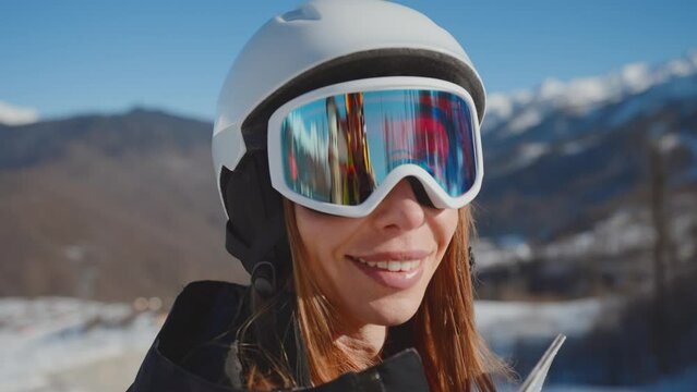 Close-up portrait of smiling woman snowboarder skyer in ski helmet and glasses in mountains, side view. Girl wearing in ski clothes in winter resort. Enjoy healthy active rest, snowboarding lifestyle.