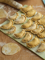 Preparing dumplings: A vertical close-up of Ukrainian varenyky on a cutting board, arranged in three rows. Dough circles are visible, with flour scattered across the table.