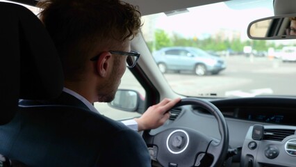 Young man driving the car in the city, looking carefully at the road. Back view. Transport, business and people concept. Real time