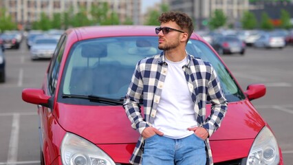 Handsome young man in eyeglasses posing near his car outdoors and showing thumb up. Trip, transportation, vacation, lifestyle concept. Real time