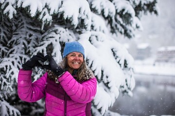 Fototapeta premium A happy middle aged woman making a heart with her hands on cold and snowy day in Colorado, USA
