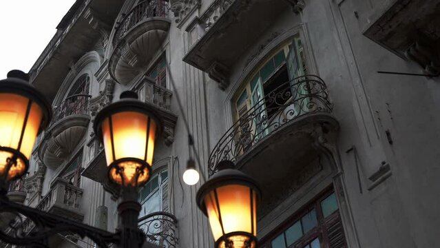 Walking and looking up through illuminated street lamp to the facade of old building with balconies in colonial style. El Conde street, Santo Domingo