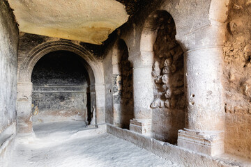 Ancient arched interiors of a Cavusin cave church, worn stone columns and faded frescoes, history,...