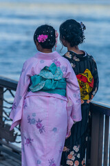 Two girls in bright kimonos stand on the banks of the Sumida River flowing in Tokyo