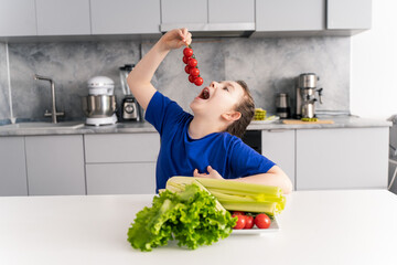 A little girl in her pre-teens with her mouth open prepared to eat cherry tomatoes. Against the...