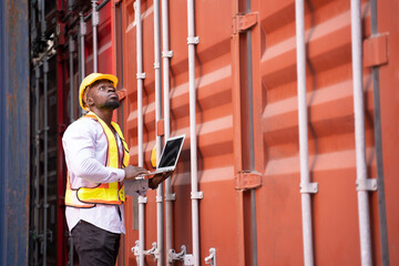 black african man wears hardhat and vest holding laptop computer checking electronic seal on container cargo,young male technician working in shipping yard,concept of container cargo shipping,industry