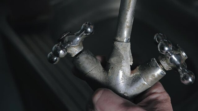 The plumber turns over an old, rusty, kitchen faucet in his hands