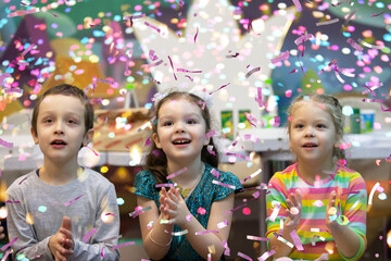 Happy, cheerful children at a children's party clap their hands and look at the flying confetti.