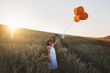 Child, letter and balloons or happy in field for communication, wish and message to the sky for fantasy with portrait. Girl, kid and paper in cornfield with travel, innocent and smile with sunlight - Powered by Adobe