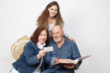 A family portrait of parents and an adult daughter looking at a photo album on a gray background.