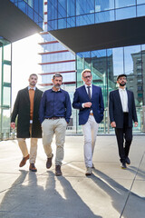 Wide vertical shot of four businessmen walking with determination outside financial district. Confident executive people concept. Copy space.