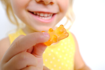 cheerful small child holds sweets, blonde girl 3 years old wants eat gelatinous candy with smile,...