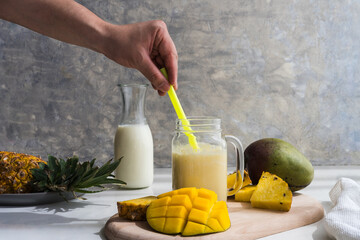 hand stirring an mango and pineapple smoothie with a straw