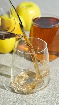 Apple juice pouring from jug into glass on gray background, slow motion
