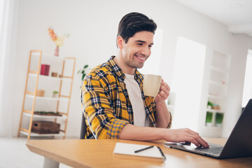 Photo of cool man wear checkered shirt drinking coffee chatting twitter telegram facebook indoors...