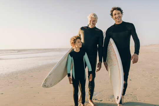 Multi generational family of men with surfboards walking on beach