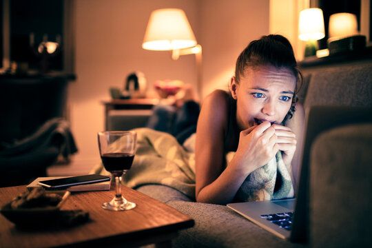 Young woman watching thriller movie on laptop at home