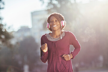 Joyful African American woman jogging in sunlight with headphones