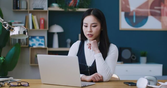 Asian manager or freelancer feeling euphoric while getting good offer with new project or salary increase. Girl loudly exclaiming words of joy and smiling broadly while sitting at table with laptop.