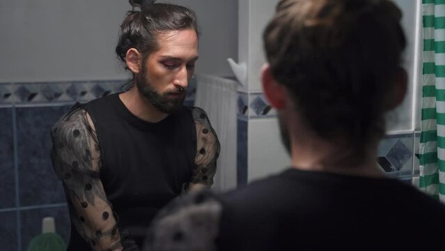 Man reflected in the mirror primping with make-up. Gay transgender LGBT person at home 