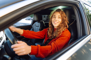 Naklejka premium Beautiful Smiling woman driving car, attractive girl sitting in automobile. Young traveler driving. Car travel, lifestyle concept.