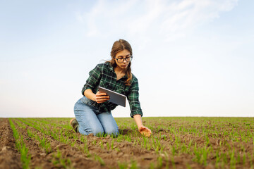 Smart farmer woman agronomist checks young sprout the field with tablet. Intelligent agriculture and digital agriculture.